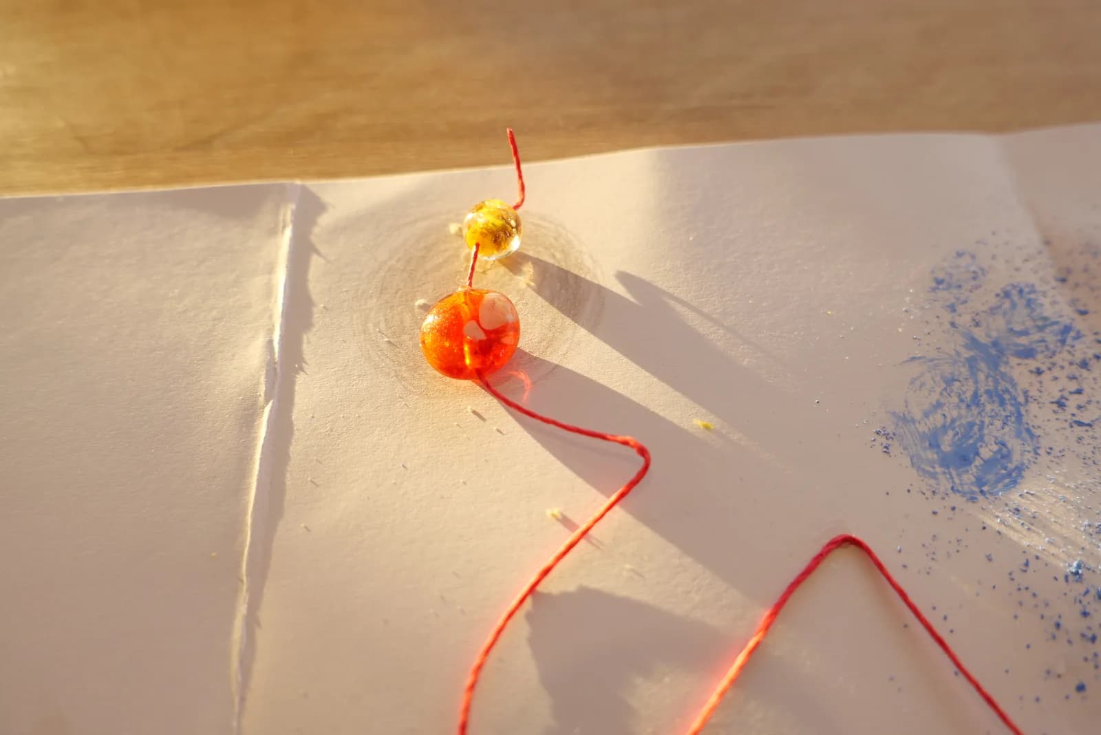 Amber-coloured beads and red thread on paper at the Inner maps workshop.