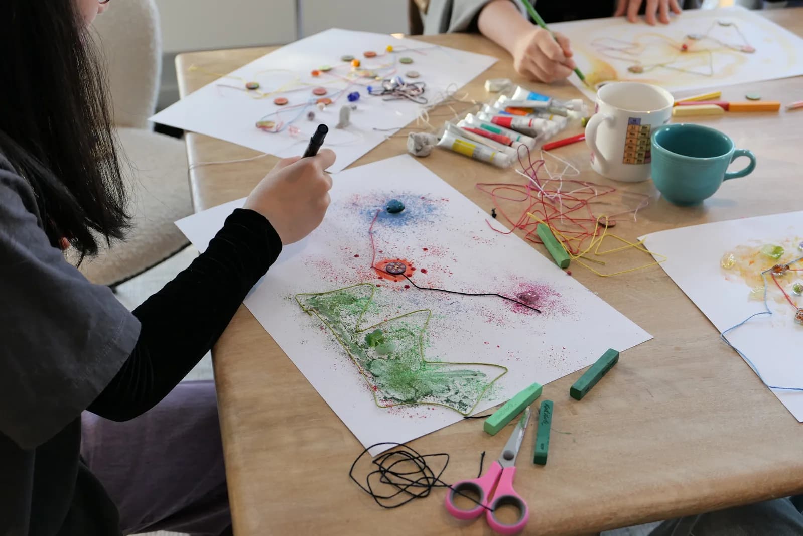 Hands working with pastels and thread at the workshop table.